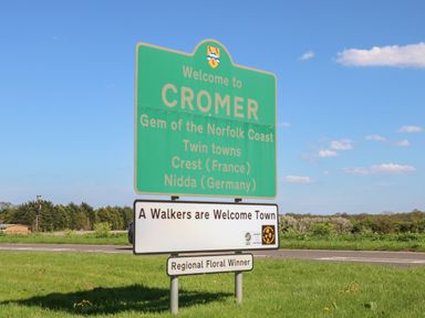 A road sign welcoming to Cromer mentioning twin towns and walkers welcome on a grassy roadside at Pebbles in Cromer