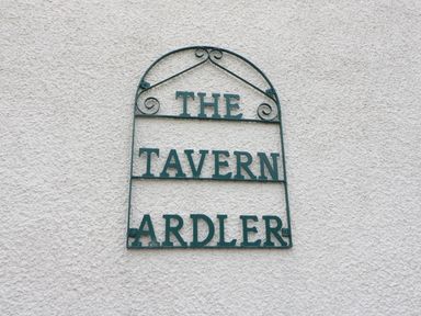 A metal sign on a textured wall reading The Tavern Ardler