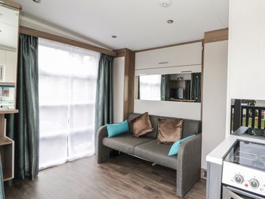 A living room with a gray sofa with cushions near a window and a kitchen stove at Cabin at the Tavern in Coupar Angus