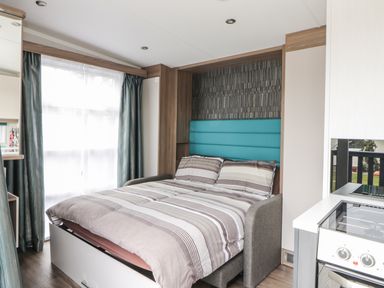 A bedroom with a double bed next to a window and a kitchen counter with stove at Cabin at the Tavern in Coupar Angus