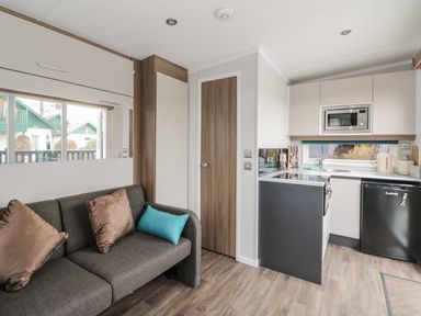A small living area with a gray sofa and pillows next to a compact kitchen with appliances at Cabin at the Tavern in Coupar Angus