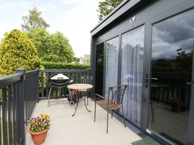 An outdoor balcony with a table chairs a barbecue grill and potted flowers at Cabin at the Tavern in Coupar Angus