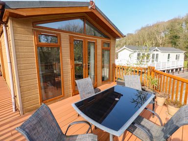 An outdoor deck with a glass table and four chairs next to a wooden cabin with large windows and a door at Jules @ 79 Stepaside