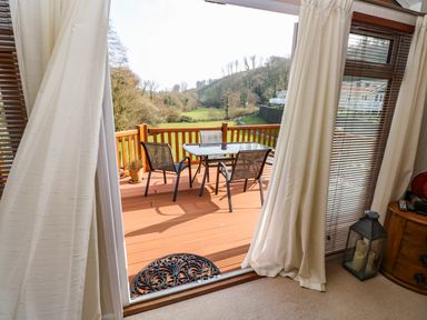 A view through a sliding door to a wooden deck with table and chairs and a grassy landscape beyond at Jules @ 79 in Stepaside