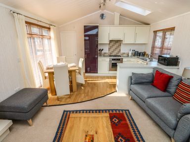 A living area with a grey sofa and ottoman a dining table with four chairs and a kitchen with white cabinets and appliances at Jules @ 79 in Stepaside
