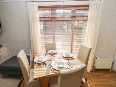 A dining area with a wooden table set for four and cream chairs near a window with blinds and curtains at Jules @ 79 in Stepaside