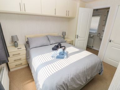 A bedroom with a double bed gray bedding two bedside tables with lamps and a view into a small bathroom at Jules @ 79 Stepaside