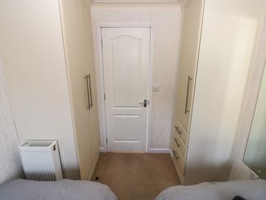 A small room with a white door between two wardrobes and a radiator on the left with beige carpet at Jules @ 79 in Stepaside