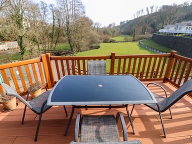 A wooden balcony with a glass table and four chairs overlooking a grassy area with trees and fences at Jules @ 79 in Stepaside