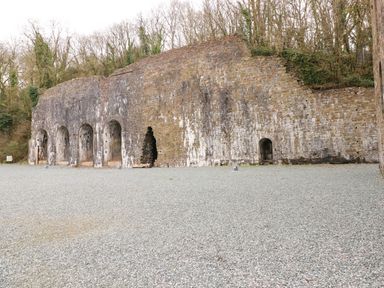 An old stone wall with multiple arches and a gravel ground surrounded by trees at Jules @ 79 in Stepaside