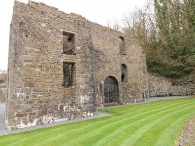 A stone ruin wall with arched and rectangular openings beside a striped grass lawn and trees in the background at Jules @ 79 in Stepaside