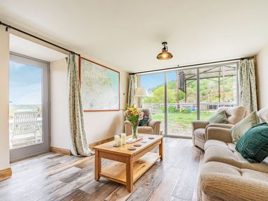 A living room with a wooden coffee table candles and flowers two armchairs and a sofa with cushions a large map on the wall glass sliding doors and a door leading outside at Meadowsweet in Goathland