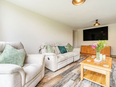 A living room with beige sofas green cushions a wooden coffee table with flowers and a large wall mounted television at Meadowsweet Goathland