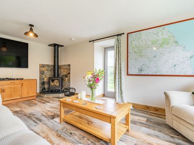 A living room with a wooden coffee table flowers on it a wood burning stove and a large wall map at Meadowsweet in Goathland