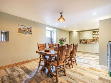 A dining area with a wooden table and six chairs next to a kitchen with cabinets and a tiled backsplash at Meadowsweet in Goathland