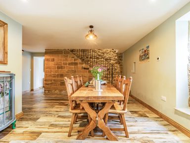 A dining room with a wooden table and chairs near a staircase with stone walls at Meadowsweet in Goathland