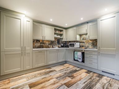 A kitchen with gray cabinets a tiled backsplash a microwave on the counter and wood patterned flooring at Meadowsweet in Goathland