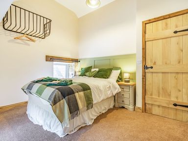 A bedroom with a bed with green pillows and a checkered blanket a small window wooden door and a bedside table with a lamp at Meadowsweet in Goathland