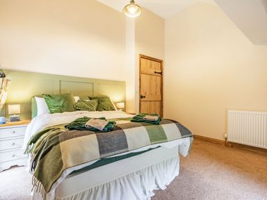 A bedroom with a bed with green pillows and blanket two bedside tables with lamps and a wooden door at Meadowsweet in Goathland