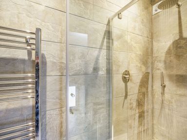 A bathroom shower area with tiled walls a glass door a metal towel rack and a showerhead at Meadowsweet Goathland