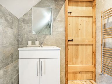 A bathroom with a white vanity cabinet sink mirror wooden door and a chrome towel radiator at Meadowsweet in Goathland