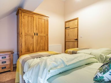 A bedroom with two beds a wooden wardrobe a wooden door and a wooden drawer unit at Meadowsweet in Goathland