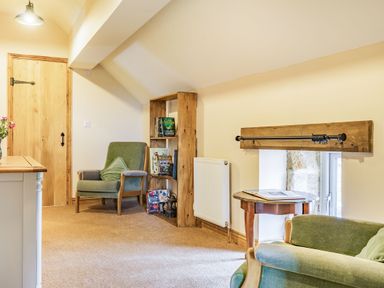 A room with green armchairs a wooden bookshelf a side table and a wooden door at Meadowsweet in Goathland