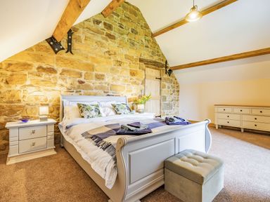 A bedroom with a stone wall bed two nightstands and a dresser at Meadowsweet in Goathland