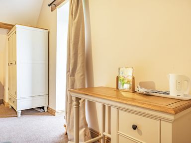 A room with a white wardrobe beige curtains and a wooden table with a small mirror and a kettle at Meadowsweet Goathland