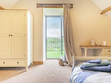 A bedroom with a wardrobe a desk a bed with folded towels and an open balcony door showing a green landscape at Meadowsweet in Goathland