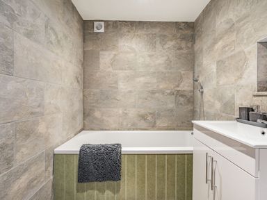 A bathroom with a bathtub, gray tiled walls, a white vanity with a sink, and a dark gray towel at Meadowsweet in Goathland