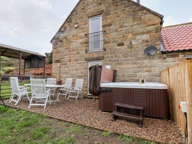 An outdoor patio area with white chairs and a table next to a hot tub by a stone building at Meadowsweet in Goathland