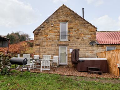An outdoor patio area with a barbecue grill table and chairs and a hot tub beside a stone house at Meadowsweet in Goathland