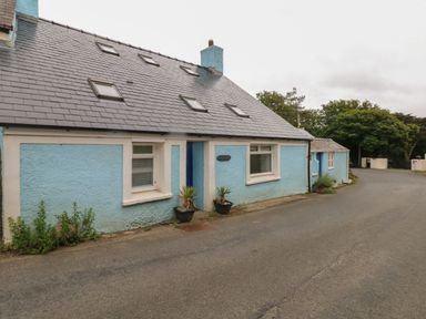 A blue painted house with small windows and a sloped roof beside a paved road at Pant y FFynnon in St Davids