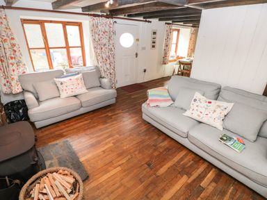 A living room with two sofas a basket of firewood and wooden floors at Pant y FFynnon in St Davids