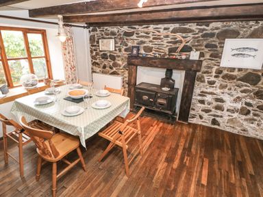 A dining room with a wooden table set with dishes and glasses near a stone wall with a wood stove at Pant y FFynnon in St Davids