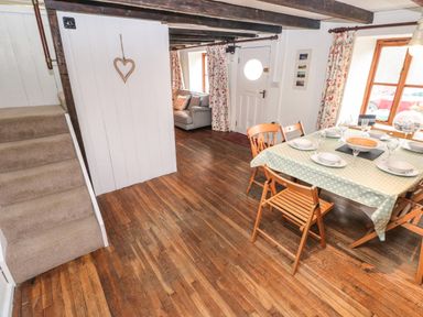 A dining area with a table set for six and wooden chairs next to a window in a room with wooden floors and exposed ceiling beams at Pant y FFynnon in St Davids