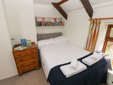 A bedroom with a double bed and folded towels on it a wooden chest of drawers with books on top and a small bookshelf above the bed at Pant y FFynnon in St Davids