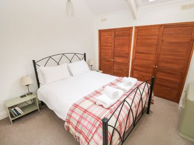A bedroom with a double bed metal frame two bedside tables with lamps wooden wardrobes and a checked blanket on the bed at Pant y FFynnon in St Davids
