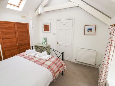A bedroom with a double bed with folded towels on a checked blanket a closet with wooden doors a small chest of drawers a door a radiator and a window with floral curtains at Pant y FFynnon in St Davids