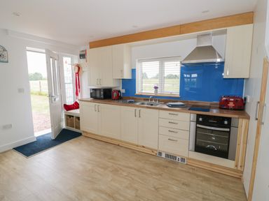 A kitchen with wooden floor white cabinets blue backsplash and door leading outside at Buttercups at Midway in Kington
