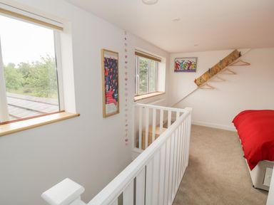 A hallway with two windows a railing wall art coat hooks and a bed with a red bedspread at Buttercups at Midway in Kington