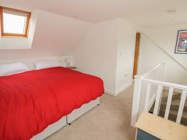 A bedroom with a bed with red bedding a small bedside table and lamp a skylight window and stairs at Buttercups at Midway in Kington