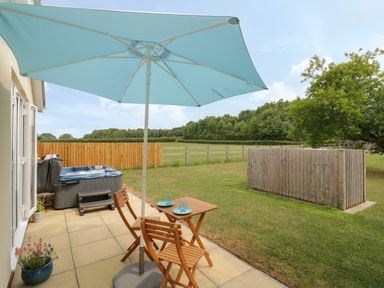 A patio with wooden chairs, table, blue umbrella, hot tub, and garden at Buttercups at Midway in Kington