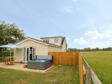 A patio with a hot tub and outdoor table and chairs next to a cream house and wooden fence at Buttercups at Midway in Kington