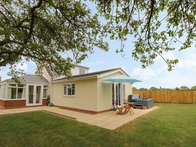 A garden with patio furniture umbrella and hot tub next to a yellow house at Buttercups at Midway in Kington