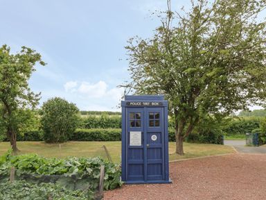 A blue police public call box outdoors near trees and a garden at Buttercups at Midway in Kington