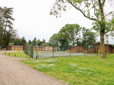 A fenced tennis court near wooden cabins surrounded by trees and grass at Great Leap in Louth