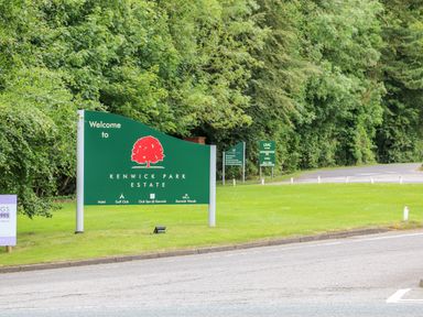 A green welcome sign for Kenwick Park Estate on grass beside a road with trees in the background at Great Leap in Louth