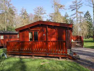 A wooden cabin with a small porch and fence surrounded by trees and grass at Great Leap in Louth